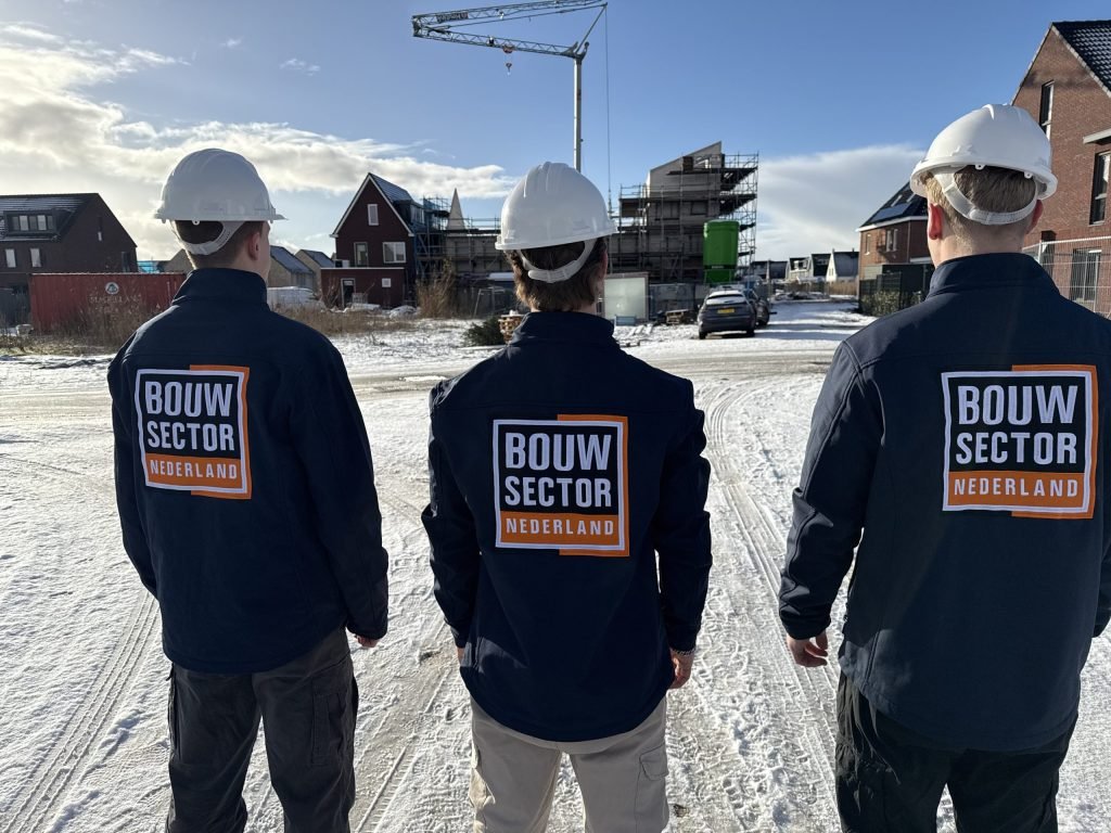 Drie vakmensen van Bouwsector Nederland met witte helm kijken naar een rij woningen in aanbouw